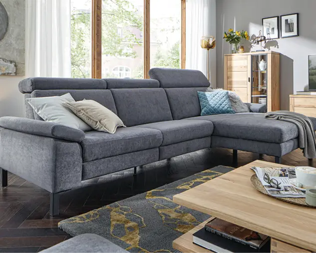 Modernes Wohnzimmer mit grauem Ecksofa, Couchtisch aus Holz und passenden Wohnmöbeln vor großen Fenstern als Beispiel für komfortable Wohnraumgestaltung